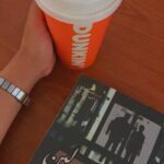 Top-down view of a mystery novel, a hand on a desk, and a cup of coffee.